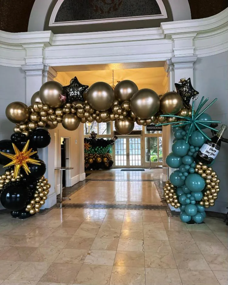 Gold, black and teal balloon garland over a hall doorway, with starbursts and Happy New Year foils
