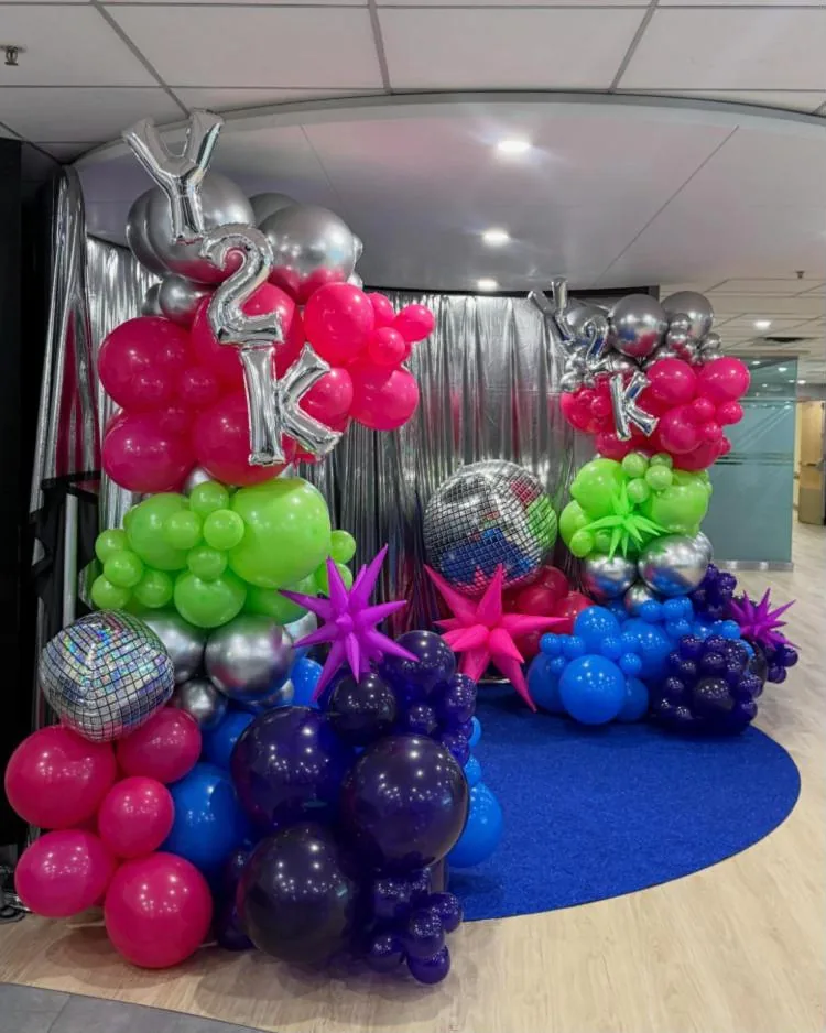 Pink, lime, blue and purple balloon columns with silver foil letters, starbursts and mirror balls in front of a silver fringe backdrop