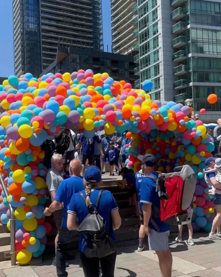 Fans walking through a rainbow balloon tunnel on a downtown Toronto plaza