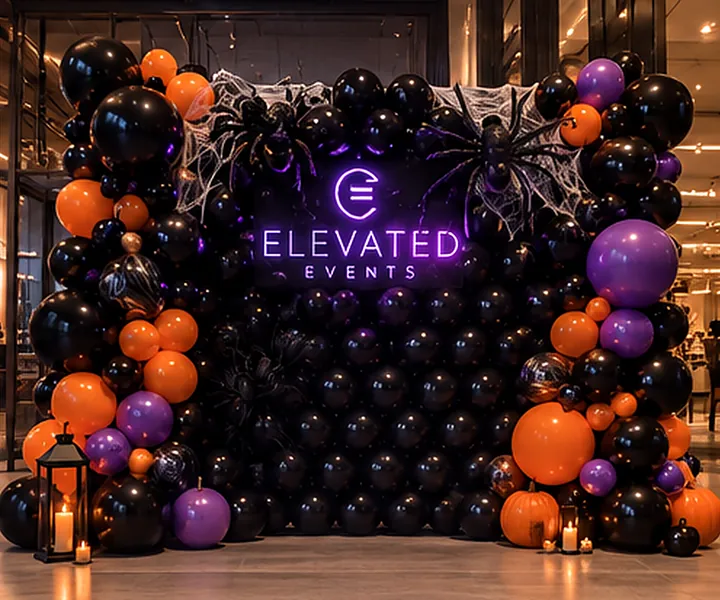 Design concept: black balloon wall with orange and purple garland, spiders and webbing, and a purple neon logo, shown with the Elevated Events logo